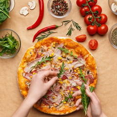 Chef adding rocket salad to pizza, top view
