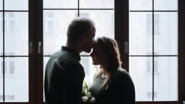 Pregnant family young husband and wife silhouette tenderly kissing by window