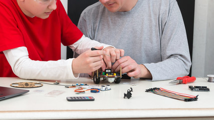 A teenager boy with his dad teacher collects a handmade metal and plastic robot. STEM education for...