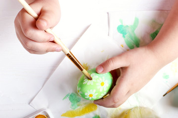 Obraz na płótnie Canvas Kid hand painted Easter eggs, paints and brushes on a white table. Preparation for the holiday. Girls hands draw a pattern.
