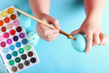 Kid hand painted Easter eggs, paints and brushes on a blue background. Preparation for the holiday. Girls hands draw a pattern.