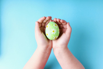 Children's hands hold a decorated Easter egg, on a blue background.