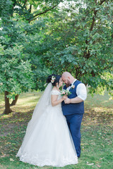 Newlyweds on their wedding day are walking in the park, looking at each other, smiling.