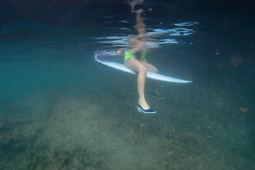 Fototapeta na wymiar Surf girl sitting on a surfboard with shoes underwater
