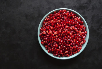 Grains of red pomegranate in a plate on a black.