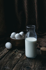 Moody, dark, rustic composition of eggs in pottery with a bottle of milk on a wooden table 