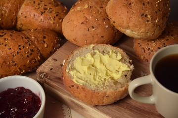 Whole grain bread and rolls with butter on the table with a cup of coffee and lingonberry jam.