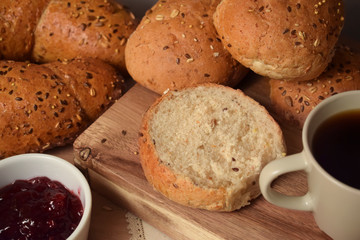 Whole grain bread and buns on the table with a cup of coffee and lingonberry jam. Close up breakfast food