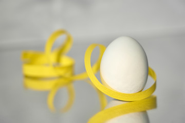                                A white egg with yellow ribbon on a silver reflective background. Easter concept. Copy space.