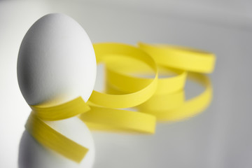                                A white egg with yellow ribbon on a silver reflective background. Easter concept. Copy space.
