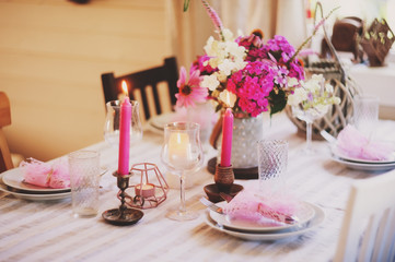 summer festive table setting in beautiful country house. Table decorated with pink flowers and candles.