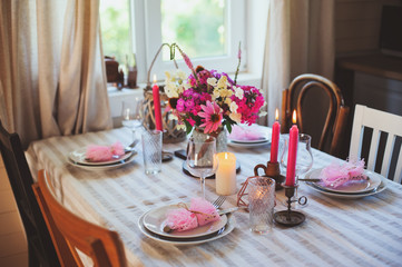 Evening dinner at home. Summer festive table setting in beautiful country house. Table decorated with pink flowers and candles.