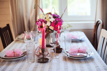 Evening dinner at home. Summer festive table setting in beautiful country house. Table decorated with pink flowers and candles.