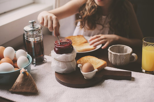 Happy Kid Girl Having Breakfast At Home, Eating Toast With Jam And Eggs On Farmhouse Kitchen