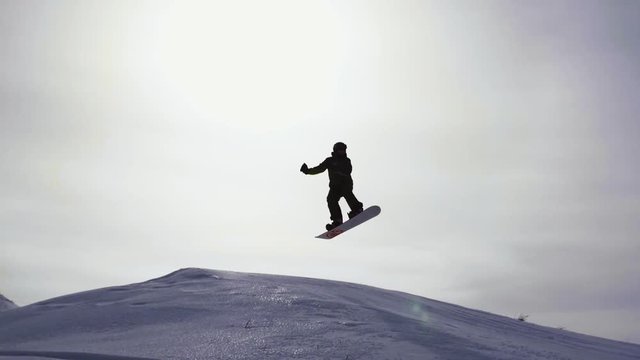 Silhouette of snowboarder jumping on mountain ski slope.