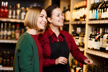 Photo of two smiling women on blurred background of shelves with bottles of wine