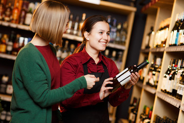 Picture of two women with bottle of wine in store on background of shelves