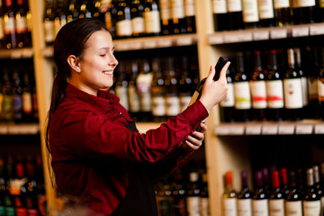 Image of young woman with bottle in her hands in wine shop