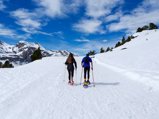 couple of excursionists walking on snowshoes and stick poles on the white snow of the winter of a path of a snowy mountain
