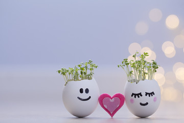 Two eggshells smiley faces with cress sprouts and pink heart. Easter eggshell planters