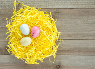 three speckled Easter eggs nestled in yellow Easter grass on a wooden table with copy space