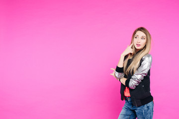 Stylish teen girl wearing in fashionable jeans and jacket posing and confident looking at camera. Blonde woman with perfect skin and natural make up standing with crossed hands in pink studio.
