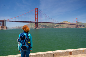 Young woman wearing backpack is watching Golden Gate bridge from the pier in San Francisco, United States on America