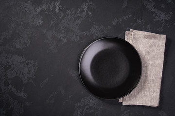 Empty black plate and napkin on a black background, top view.