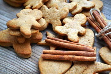Gingerbread cookies in shapes of heart, star and man with cinnamon stick and ginger root on wooden table