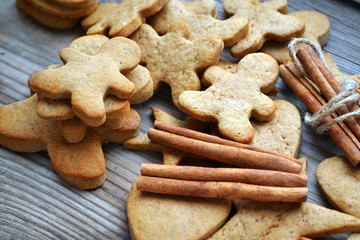 Gingerbread cookies in shapes of heart, star and man with cinnamon stick and ginger root on wooden table