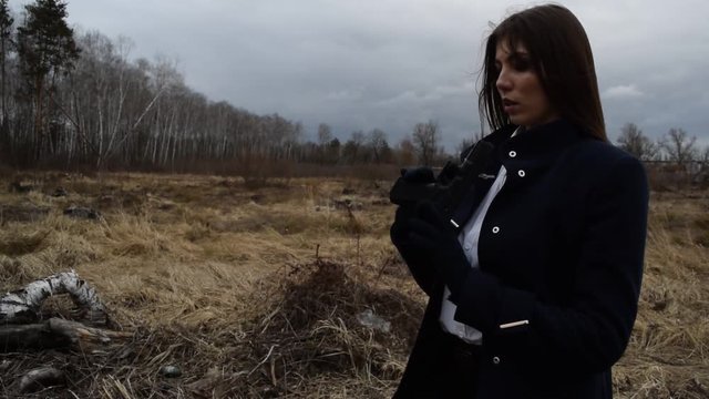 Young brunette girl shoots with a gun in a coat on the field.