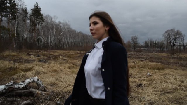 Young brunette girl with a gun in a coat dry on the field in cloudy weather.