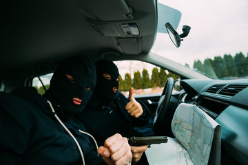 Bank robbers with their masks on pointing at the map prepared for robbing the bank,sitting in the car and waiting for the right time to rob.