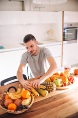 Young and healthy man putting fruits in his blender early in the morning.