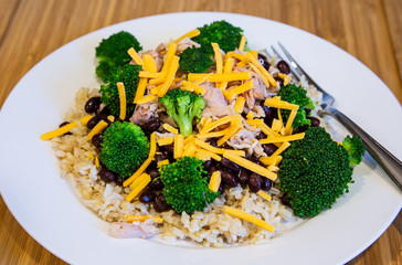 A dinner plate with Chicken Beans Broocoli Cheese and Rice and a fork