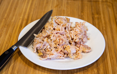 Chopped Cooked Chicken on a white plate and wood cutting board with a chefs knife