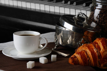 Cup of coffee with croissants on piano background