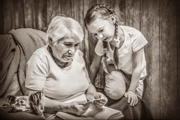 grandmother and granddaughter in a chair, watching a photo, reading a book together, precious time...