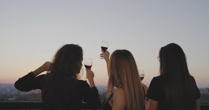 On the top of building with a amazing sunset view ladies have a wine party they admire the beautiful sunset and cheers with glass wine.