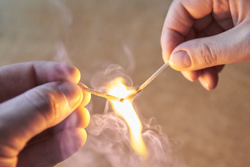 The hand of a man and a woman hold burning matches