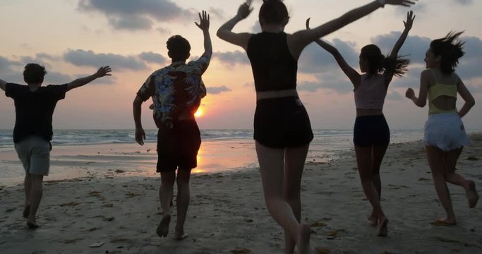 Group of Friends having fun running down the beach with sunset background. People with party celebration concept. 4K resolution. Slow motion shot.