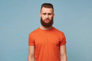 Portrait of emotional bearded man with a sad expression on face, crooked lower lip with a disgruntled look. The male received bad news, feels disappointed, isolated over blue background