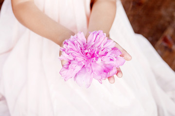 Girl holding a pink peony flower in hand. Close up picture