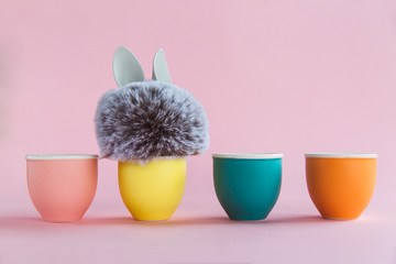 Fur ball with bunny rabbit ears in egg stand on bright background. Four egg stands. Easter minimal concept