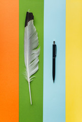 Black ballpoint pen and white feather on multicolor paper as a symbol of poetry. Writing and prose...