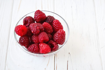 Little glass plate with raspberry on white wooden table. Healthy meal, summer fruits.