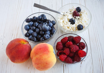 Healthy meal with organic cottage cheese, fresh raspberry, blueberry, peach on white wooden table. close up 