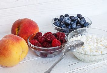 Healthy meal with organic cottage cheese, fresh raspberry, blueberry, peach on white wooden table. close up 