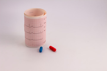 Electrocardiogram paper roll with the heart beat next to two colored pills. You can read the words sex, age, name, ID and unconfirmed.