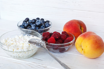 Healthy meal with organic cottage cheese, fresh raspberry, blueberry, peach on white wooden table. close up 